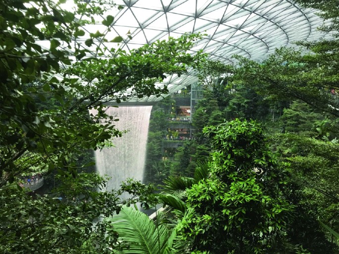 A photograph of a giant indoor waterfall from a conical structure. Trees are in the foreground.