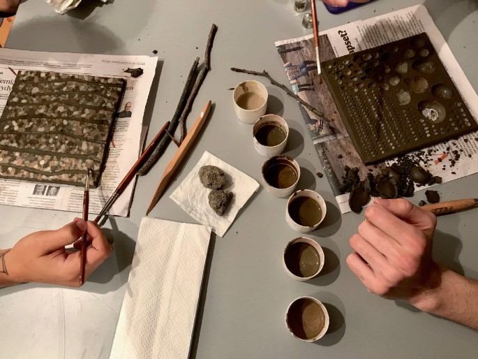 A picture depicts workshop participants working with a variety of soil that has been ground into a fine slip utilising sticks and brushes.