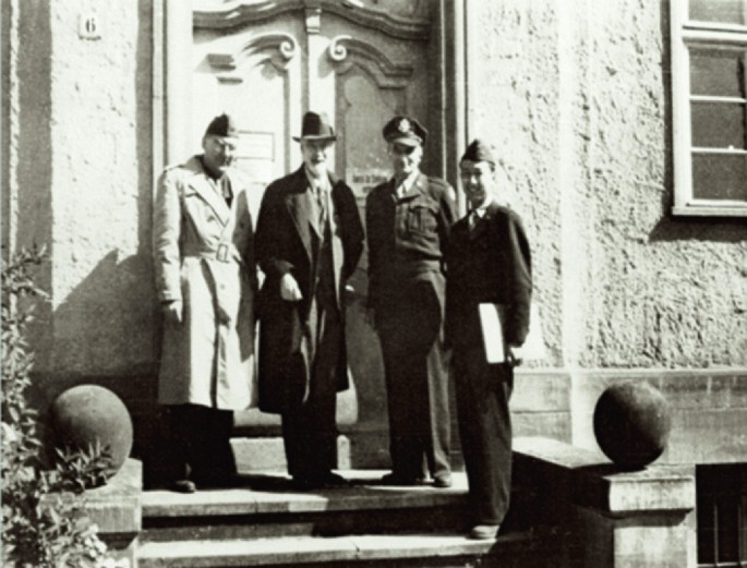 A photo of four people standing in front of the door and posing towards the camera.