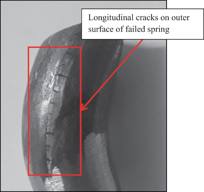 A photograph of a failed spring. The longitudinal cracks on the outer surface are boxed and pointed by an arrow.