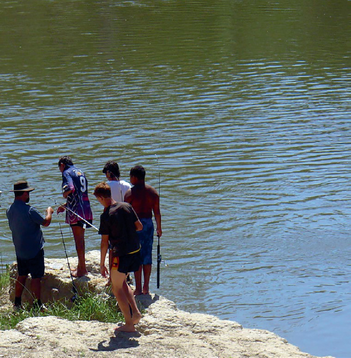 A photograph of five people ready for fishing beside a river with fishing rods.