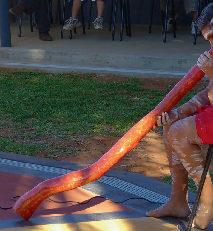 A photograph of a person playing the didgeridoo and some people seated in their respective places.