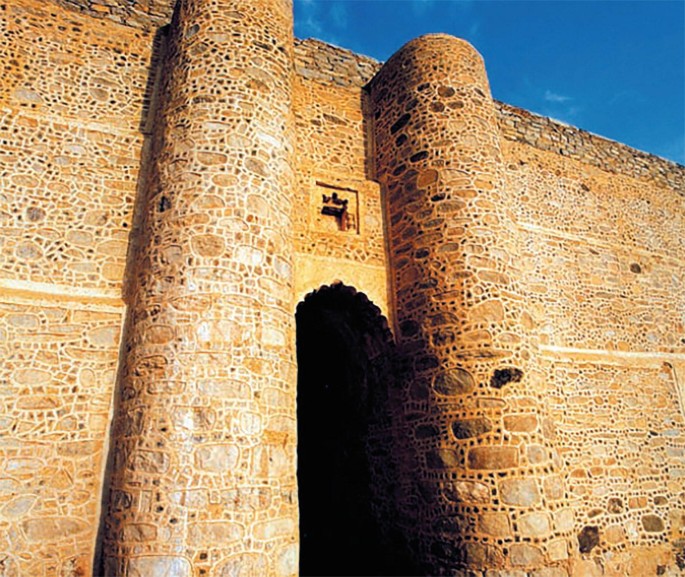 A photograph of a tall fort wall built using round edged bricks or stones. A carved entrance way leads to the dark interior.