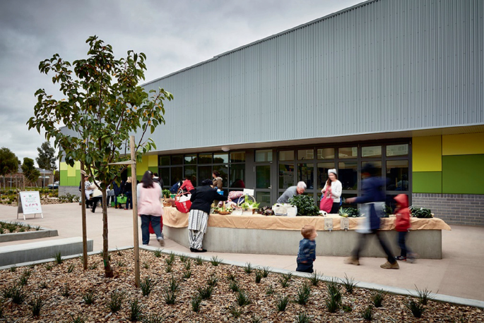 A photo of Mernda Central P-12 College with the local market in the background. Some people are purchasing goods.