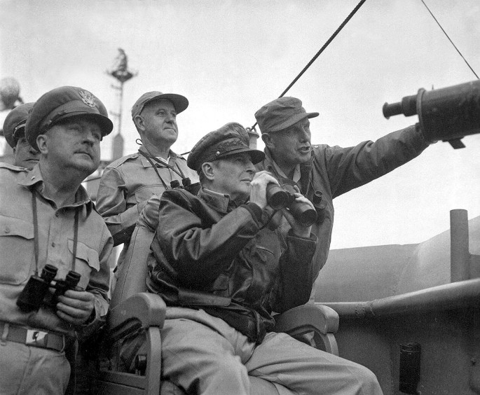 A photograph of Mac Arthur with some soldiers, observing a naval shelling of Incheon with a pair of binoculars as one man guides him.