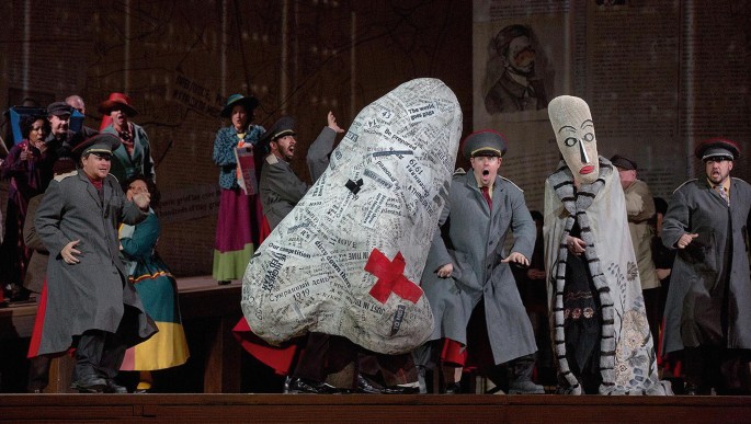 A poster of the Nose Opera illustrates a person cloaked in a garment made of newspaper cuttings, running around while the security personnel watch in awe, and another person in an elongated face mask with a big nose, stands passively.