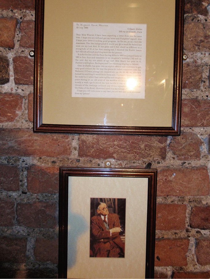 A photo of two framed items on a brick wall. A letter at the top and a portrait of James Joyce at the bottom.