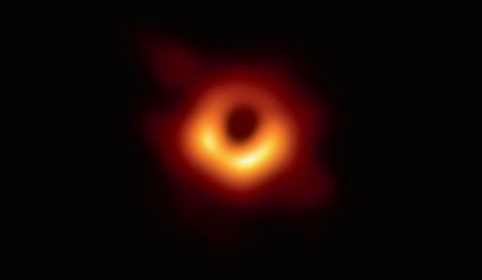 A space photograph of a M 87 galaxy surrounded by a dark cloud. The bright spot at the center has a supermassive black hole.