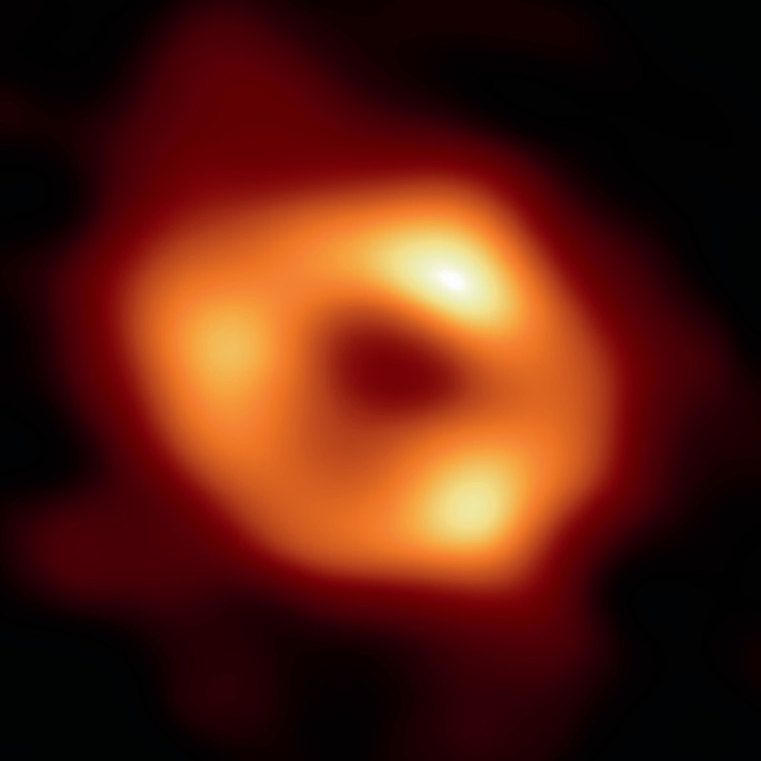 A zoomed-in space photograph of a supermassive black hole in the galaxy surrounded by a dark cloud.