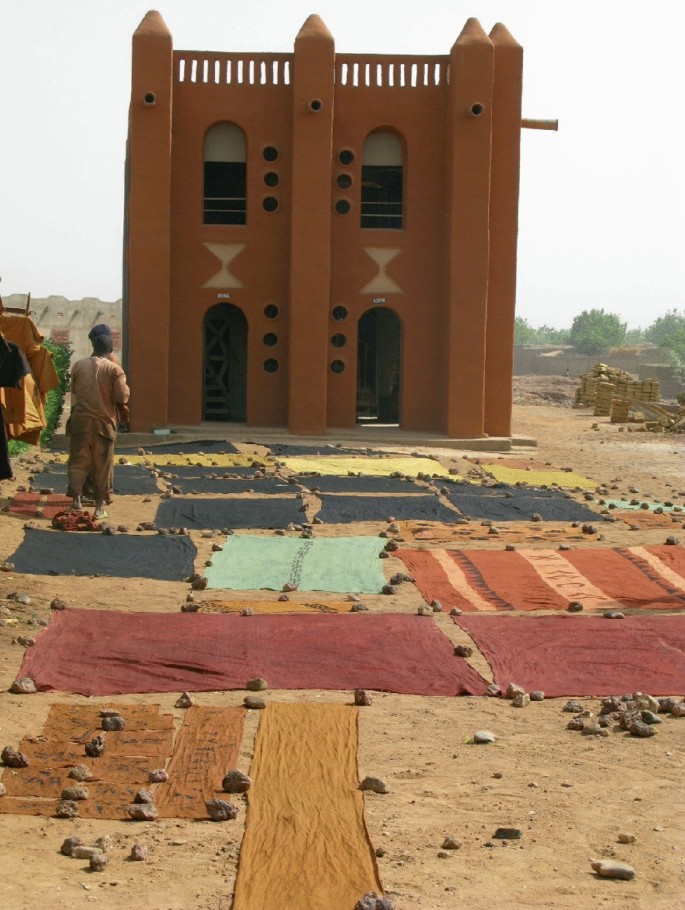 A photo of a house with pieces of fabric on the ground in front of it in daylight. The fabrics are secured with stones.