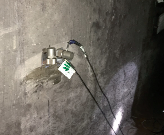 A photograph of a metallic device inserted into the wall connected to 2 long wires.