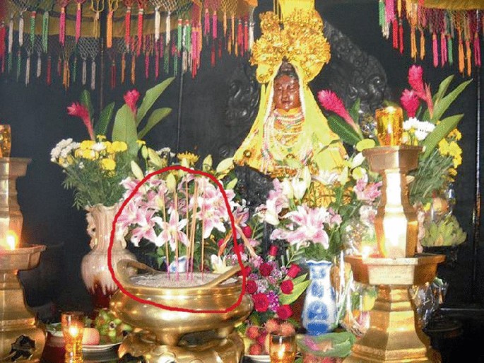 A photograph of a deity wearing gold ornaments and some golden ornaments placed around it that have colorful flowers.