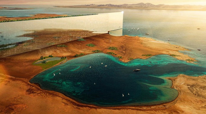 An aerial photograph depicts a tall, narrow, mirrored wall along a desert reaching the ocean. The mirrored wall reflects the desert as well as the ocean. Boats and ships are sailing in the ocean.