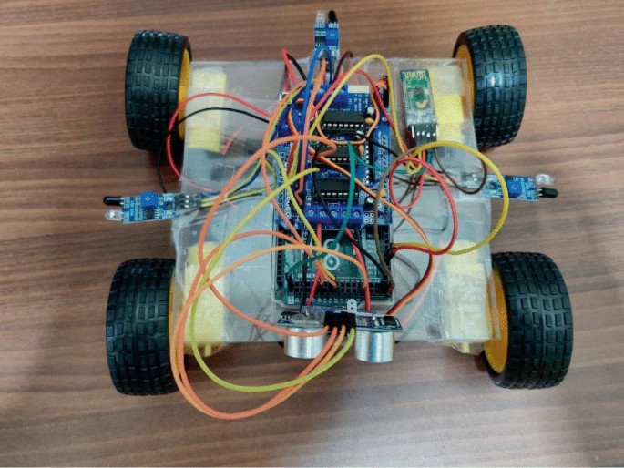 A photograph of a robot which consists of a circuit board with interconnected wires, mounted over four wheels.