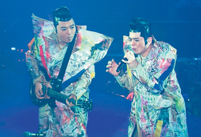 A photograph of the Tat Ming pair in a concert wearing a newspaper outfit.
