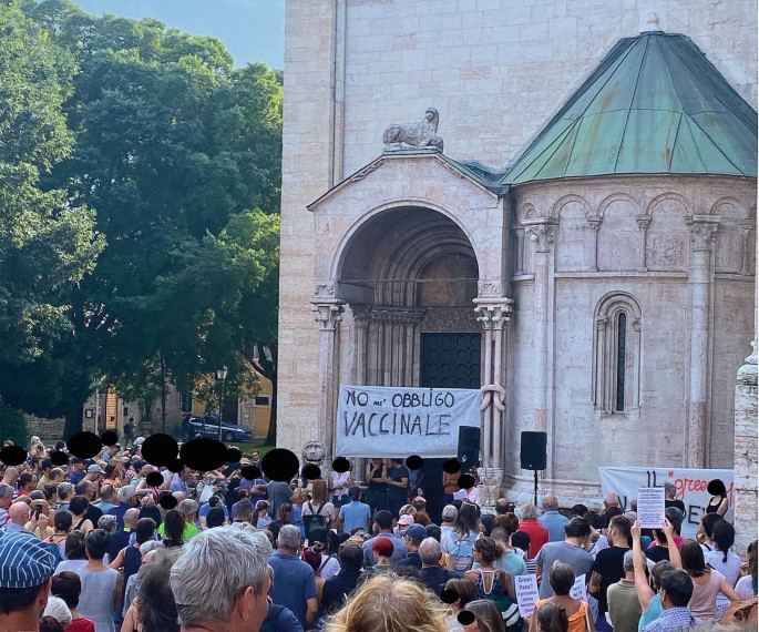 A photograph of a crowd of people protesting against anti-COVID vaccination and holding up a banner with text in a foreign language.