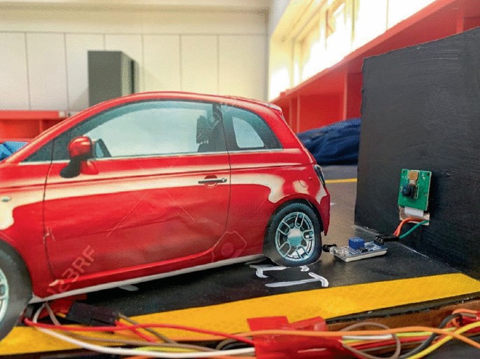 A car is connected to an electric board linked to a chip-like setup with wires on a dark board.