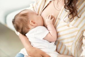 a baby breastfeeding from a woman in a white and yellow shirt