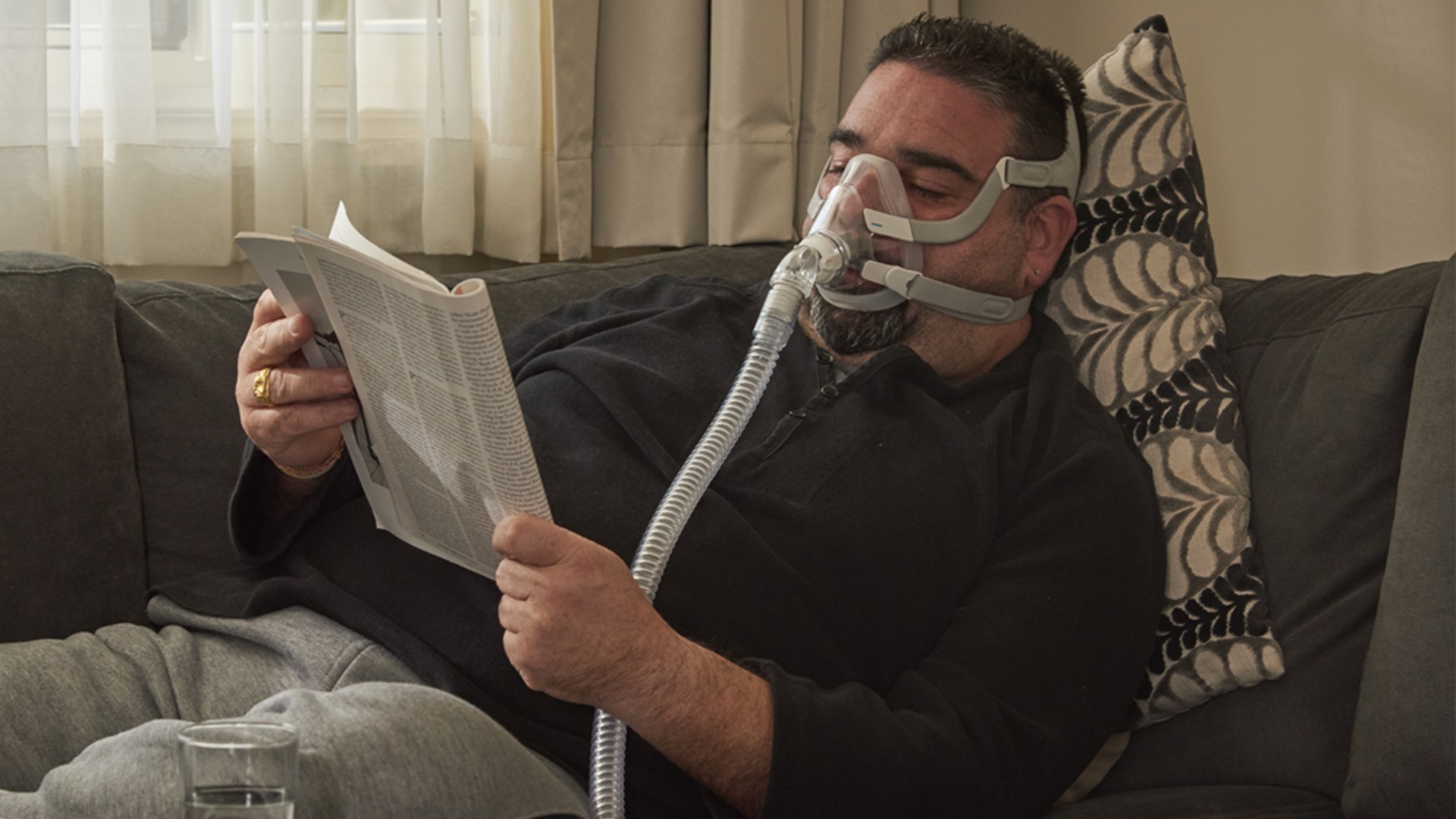Mann mit Atemmaske liest Zeitschrift auf dem Sofa