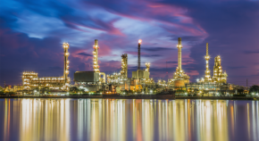 A petrochemical refinery located at the edge of a body of water illuminates the surroundings with its many bright lights at night.