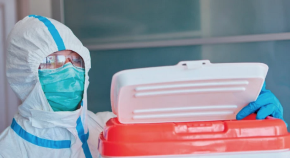 A worker in personal protective equipment opens a cooler.
