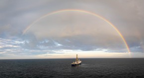 A drilling ship is seen on the ocean with a rainbow behind.