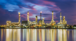 A petrochemical refinery located at the edge of a body of water illuminates the surroundings with its many bright lights at night