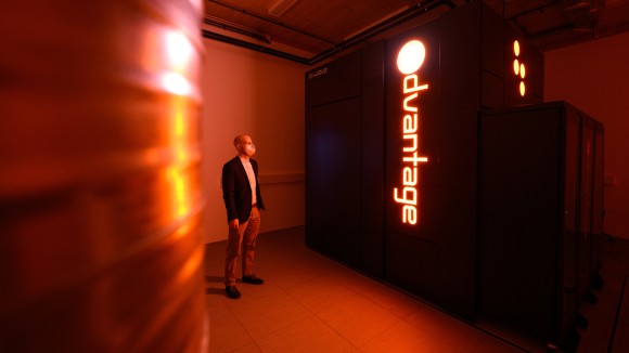 An employee stands next to the D-Wave Systems Advantage quantum computer, lit only by an orange glow.