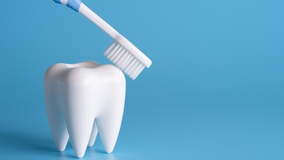White toy tooth being scrubbed by a white toothbrush in blue background.