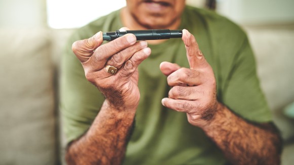 Shot of a senior man using a finger pricking device to check his blood sugar levels