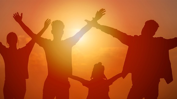 Silhouette of teenagers and a younger child raising their arms in front of an orange setting sun