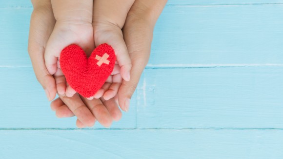 Top view of adult and child holding red heart in hands