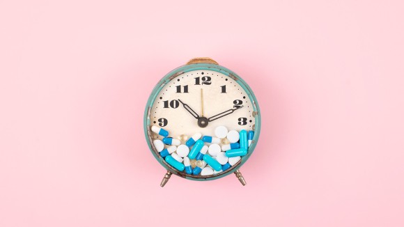 Old alarm clock with Tablets, medicine and pills on clock face on pink background. colorful capsules on clock. 