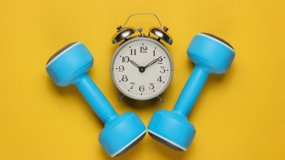 Training time! Dumbbell, alarm clock on yellow background. Minimalistic sport concept. Top view