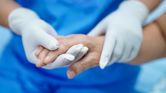 Gloved professional holding the hand of a patient