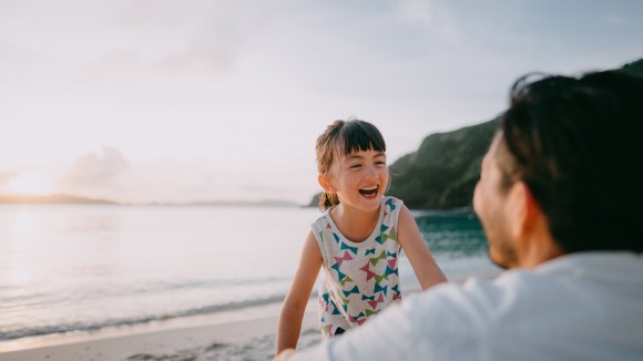 Toddler girl laughing on a beach at sunset.