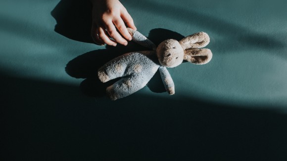 Child's hand reaches for a Small Toy Bunny, with shadows overcasting the image
