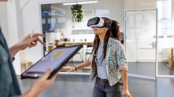 Young woman wearing virtual reality headset by a male colleague using a digital tablet. Startup business colleagues testing out virtual reality glasses in the office.