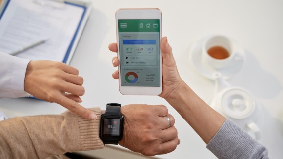 Image of wristwatch on a person's wrist. The person is also holding a mobile phone, displaying biometric information on a mobile app.