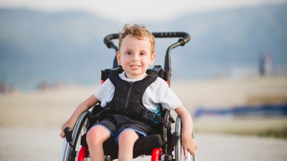 Smiling young boy on the wheelchair by the sea