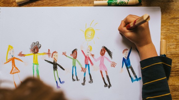 child drawing a picture of children with coloured crayons