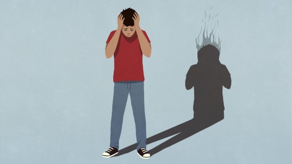 Shadow of a burning head behind a frustrated boy with his head in his hands