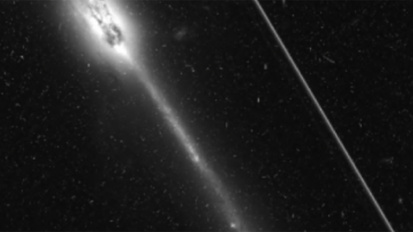 Hubble Space Telescope image of an edge-on galaxy, showing a satellite trail to the right.