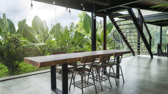 Industrial looking glass, metal and wood office space with desk in front of window behind which are tropical green plants