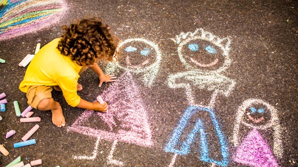 child drawing picture of children on ground with chalk