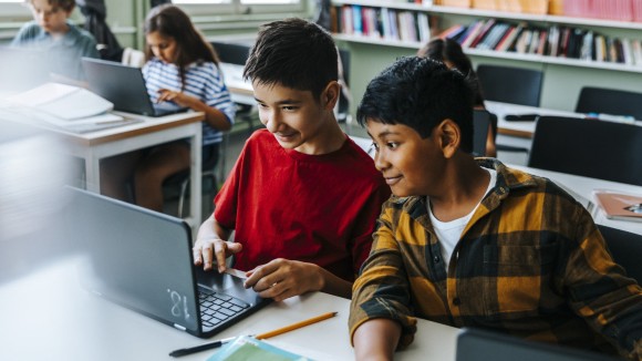 High angle view of boy studying with classmate on laptop while sitting in classroom at elementary school
