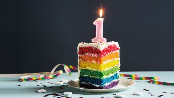 A piece of rainbow cake with the number one as candle