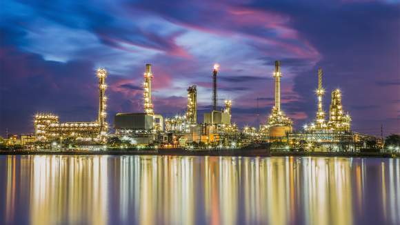 A petrochemical refinery located at the edge of a body of water illuminates the surroundings with its many bright lights at night.