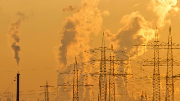 Electricity pylon in a heat haze with plumes of industrial smoke rising into an orange sky in the background