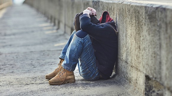 Young homeless boy sitting on pavement on a bridge, head in hands.